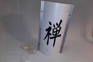 Gebroken witte tafellamp met vooraan grote zwarte Chinese tekens en op de achtergrond kleinere beige tekens 